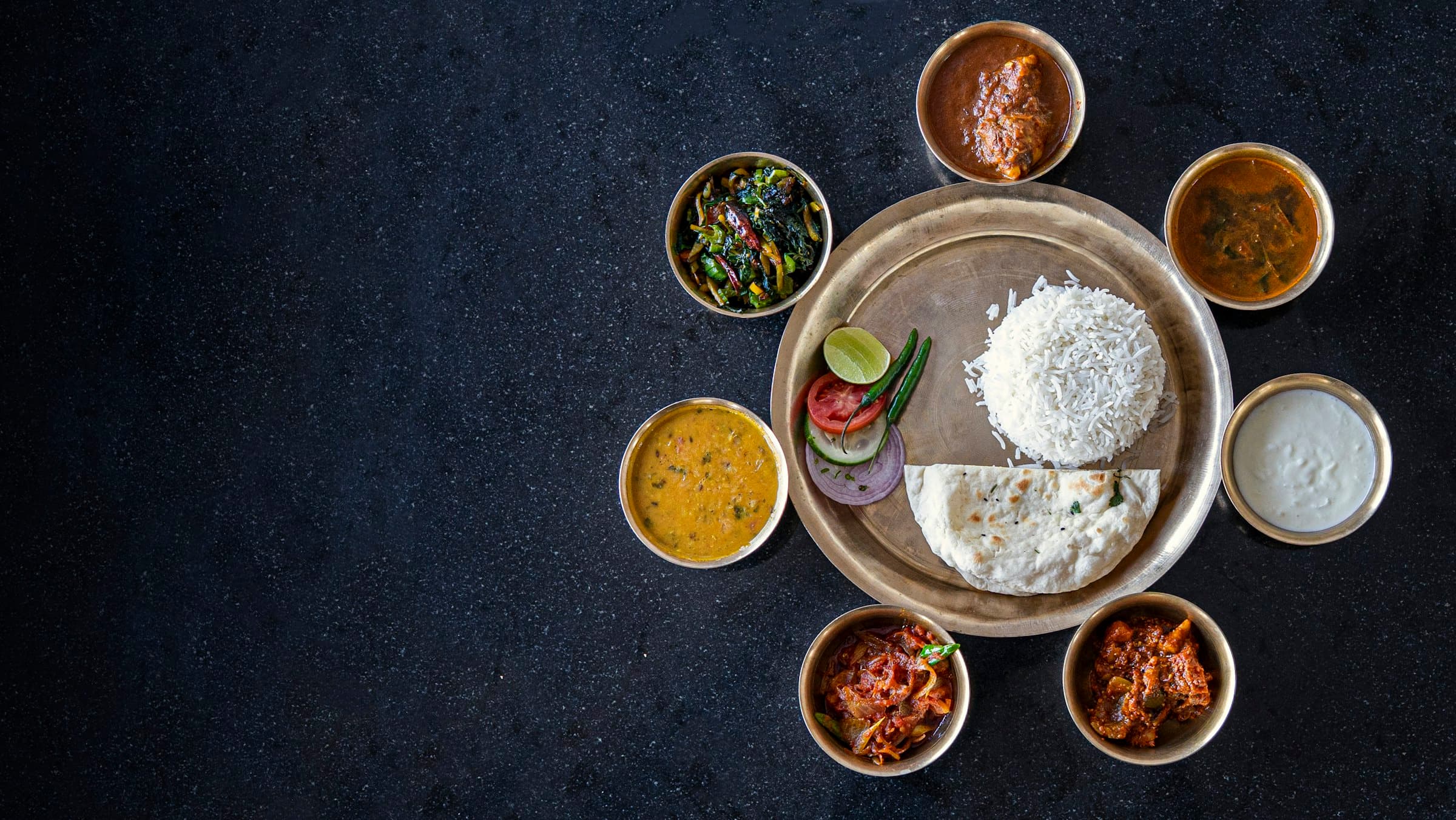 A spread of Indian dishes served in small bowls on dark slate